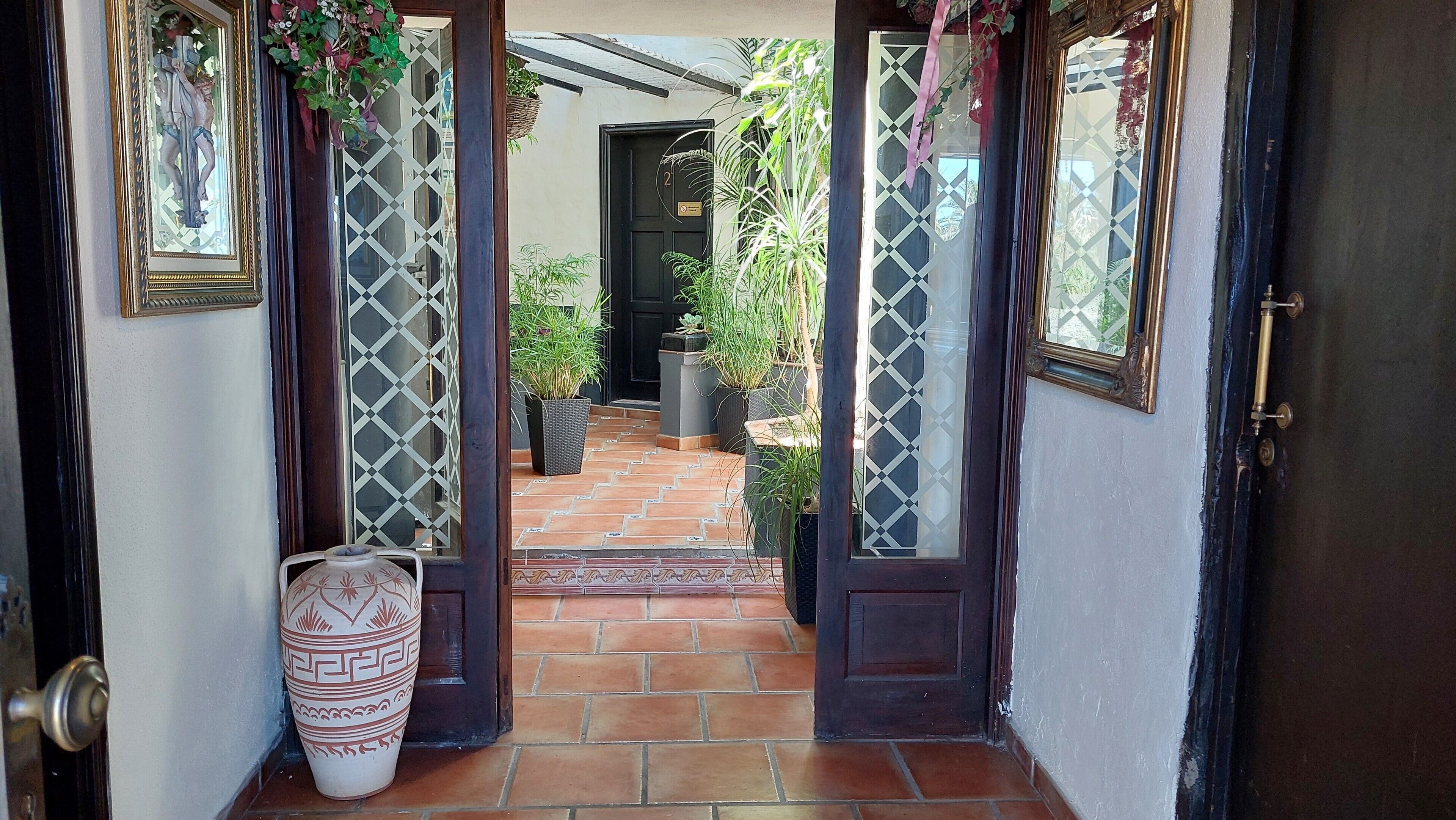 Una puerta con puertas de vidrio con diseño, un vestíbulo con baldosas y una planta en maceta.