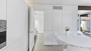 Een moderne keuken met witte kastjes, een ingebouwde oven en een eethoek met een witte tafel en stoelen.