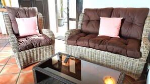 Two wicker sofas with cushions, a glass coffee table, and a potted plant.