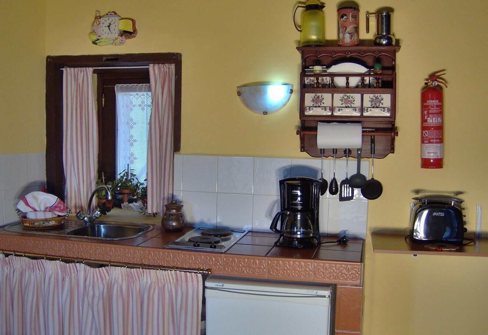 A kitchen with a sink, stove, coffee maker, and a fire extinguisher.