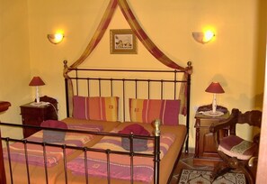 A bed with a canopy, two bedside lamps, a wooden chair, and a framed picture on the wall.