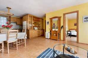 Une cuisine avec des meubles de rangement en bois, une table à manger avec des chaises, un radiateur et une table en verre agrémentée d’objets décoratifs.