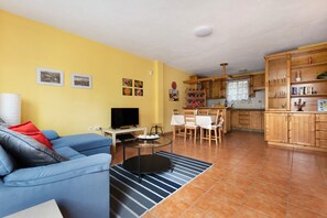 Un salon comprenant un canapé, un téléviseur et un coin repas avec des chaises et une table.