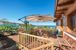 En træterrasse med et bord og stole, en stor parasol og havudsigt.