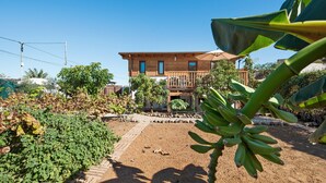 Une maison en bois dotée d’un balcon, entourée de verdure et bordée d’une zone pavée.
