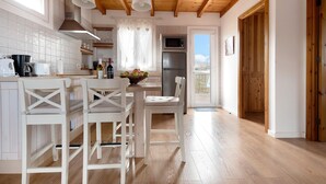 Une cuisine avec des poutres en bois, des meubles blancs et un coin repas avec des chaises blanches.