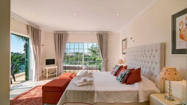 Een slaapkamer met een groot bed, een televisie, een balkon en uitzicht op groen.