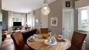 Een eethoek met een ronde houten tafel, bruine leren stoelen, een hanglamp en een televisie op de achtergrond.