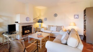 Una sala de estar con chimenea, un sofá, una mesa de centro, un televisor y una estantería.