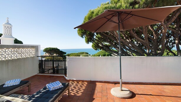 Una terraza en la azotea con dos sillones, una mesa redonda y un gran parasol.