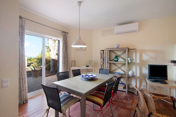 A dining area with a table, chairs, a hanging light, and a TV.