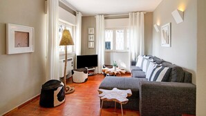 A living room with a sofa, ottoman, TV, and a lamp. - Villa 'Apple' with Sea View, Wi-Fi, and Air Conditioning (Vale do Lobo)