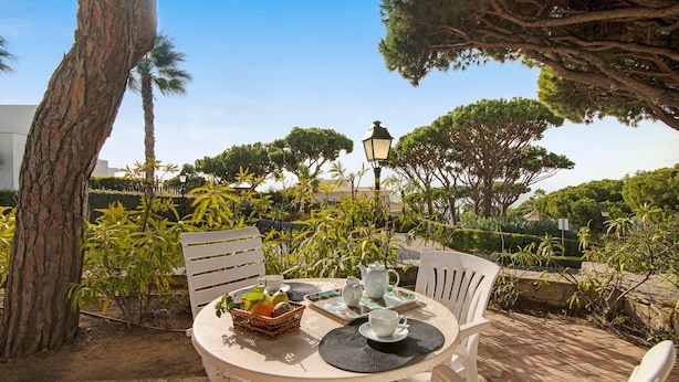 A round table with chairs, a basket of fruit, a teapot, and cups on a patio with trees and a lamp in the background. - Villa 'Apple' with Sea View, Wi-Fi, and Air Conditioning (Vale do Lobo)
