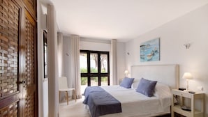 A bedroom with a bed, bedside tables, a chair, a window with curtains, and a painting on the wall. - Villa 'Harlequin' with Sea View, Wi-Fi and Air Conditioning (Vale do Lobo)
