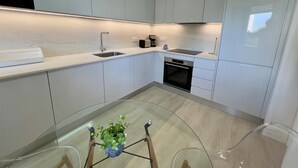 A modern kitchen with white cabinetry, a stainless steel sink, a built-in oven, and a glass table with a potted plant. - Villa 'Harlequin' with Sea View, Wi-Fi and Air Conditioning (Vale do Lobo)