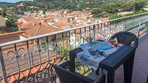Un balcone con un tavolo apparecchiato per due, affacciato su una città con tetti in terracotta e vegetazione lussureggiante.