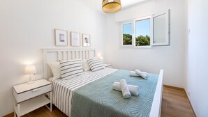 Une chambre à coucher avec un lit, une table de chevet, une lampe, des tableaux encadrés et une fenêtre.