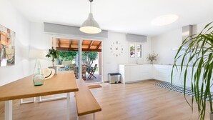 Une cuisine moderne avec des meubles blancs, une table à manger en bois et un luminaire suspendu.