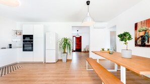 Une cuisine moderne avec des meubles blancs, une table à manger en bois et un luminaire suspendu.