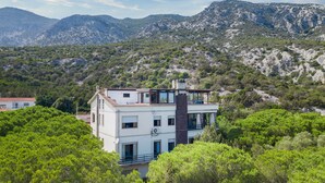 A multi-story building with balconies, surrounded by dense greenery and mountains in the background. - Apartment 'Oriente' with Private Terrace, Wi-Fi and Air Conditioning (Cala Gonone)