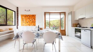 A modern kitchen with white cabinets, a dining table with chairs, and a view through large windows. - Apartment 'Oriente' with Private Terrace, Wi-Fi and Air Conditioning (Cala Gonone)