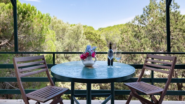 A round table with two chairs, a vase with flowers, a bottle, and a glass on the table. - Apartment 'Oriente' with Private Terrace, Wi-Fi and Air Conditioning (Cala Gonone)