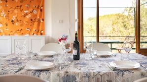 A dining table set with plates, glasses, and a bottle of wine, with a view of greenery outside. - Apartment 'Oriente' with Private Terrace, Wi-Fi and Air Conditioning (Cala Gonone)