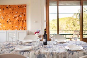 Mesa de jantar posta com pratos, copos e uma garrafa de vinho, com vista para o verde lá fora.