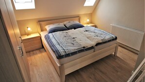 Quarto com cama de madeira, duas mesas de cabeceira com luminárias, radiador e claraboia.