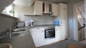 Uma cozinha compacta com armários brancos, forno embutido, cafeteira e torradeira.