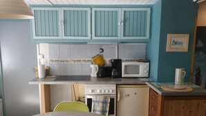 A kitchen with blue cabinets, a microwave, a stove, and a dining table with chairs. - Pleasant studio on the ground floor with private terrace and garden. 2 steps from the beach (Pornic)