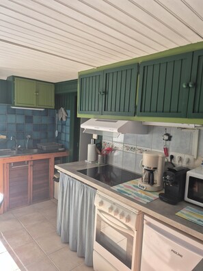 A kitchen with green cabinets, a stove, a microwave, and a coffee maker.