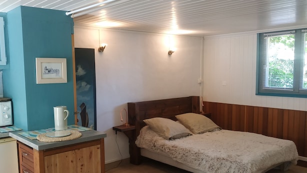A room with a bed, a desk, a chair, a window, and a wall-mounted light fixture. - Pleasant studio on the ground floor with private terrace and garden. 2 steps from the beach (Pornic)