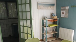 A room with a round table, green chairs, a green-framed door, a shelf with books, and a painting on the wall. - Pleasant studio on the ground floor with private terrace and garden. 2 steps from the beach (Pornic)