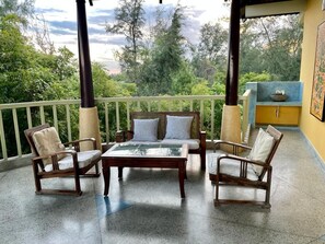 Ein Balkon mit einem Holztisch, vier Stühlen, einem gelben Schrank und Blick auf Bäume und Himmel.