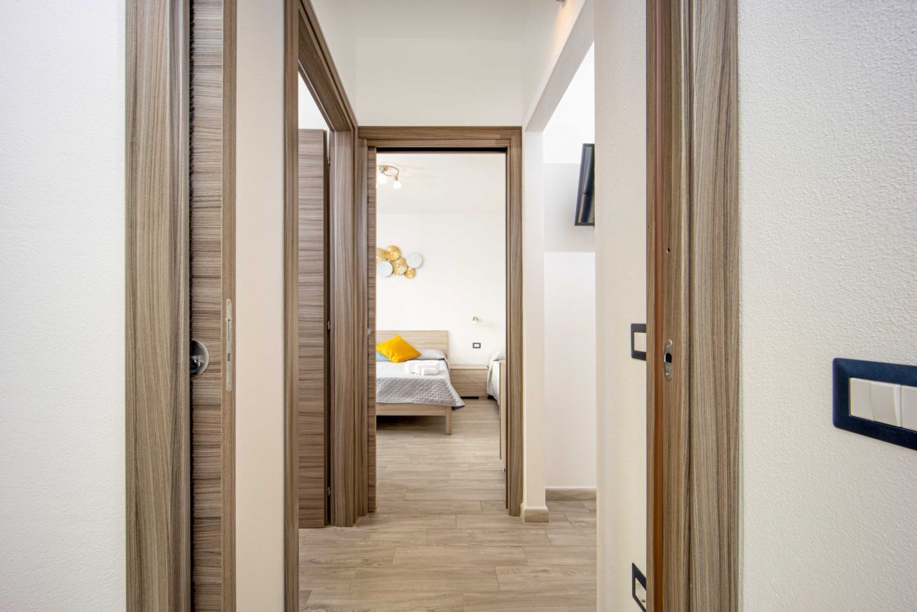 Un couloir menant à une chambre à coucher équipée d’un lit, d’une table de chevet et d’un luminaire fixé au mur.