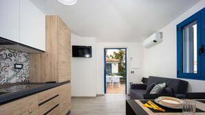 Una cocina moderna con armarios de madera y un televisor integrado. Hay un área de comedor con una mesa y sillas, y un ventanal con marco azul.