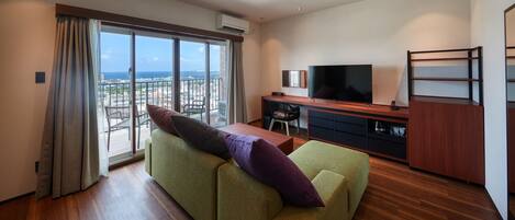 A modern living room with a large window, a flat-screen TV, a wooden desk, and a green sofa.