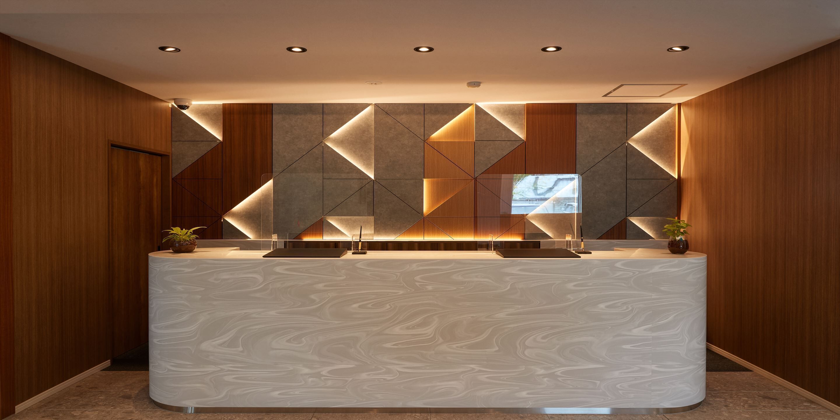 A reception desk with a marble-like surface, geometric wall design, and recessed lighting.