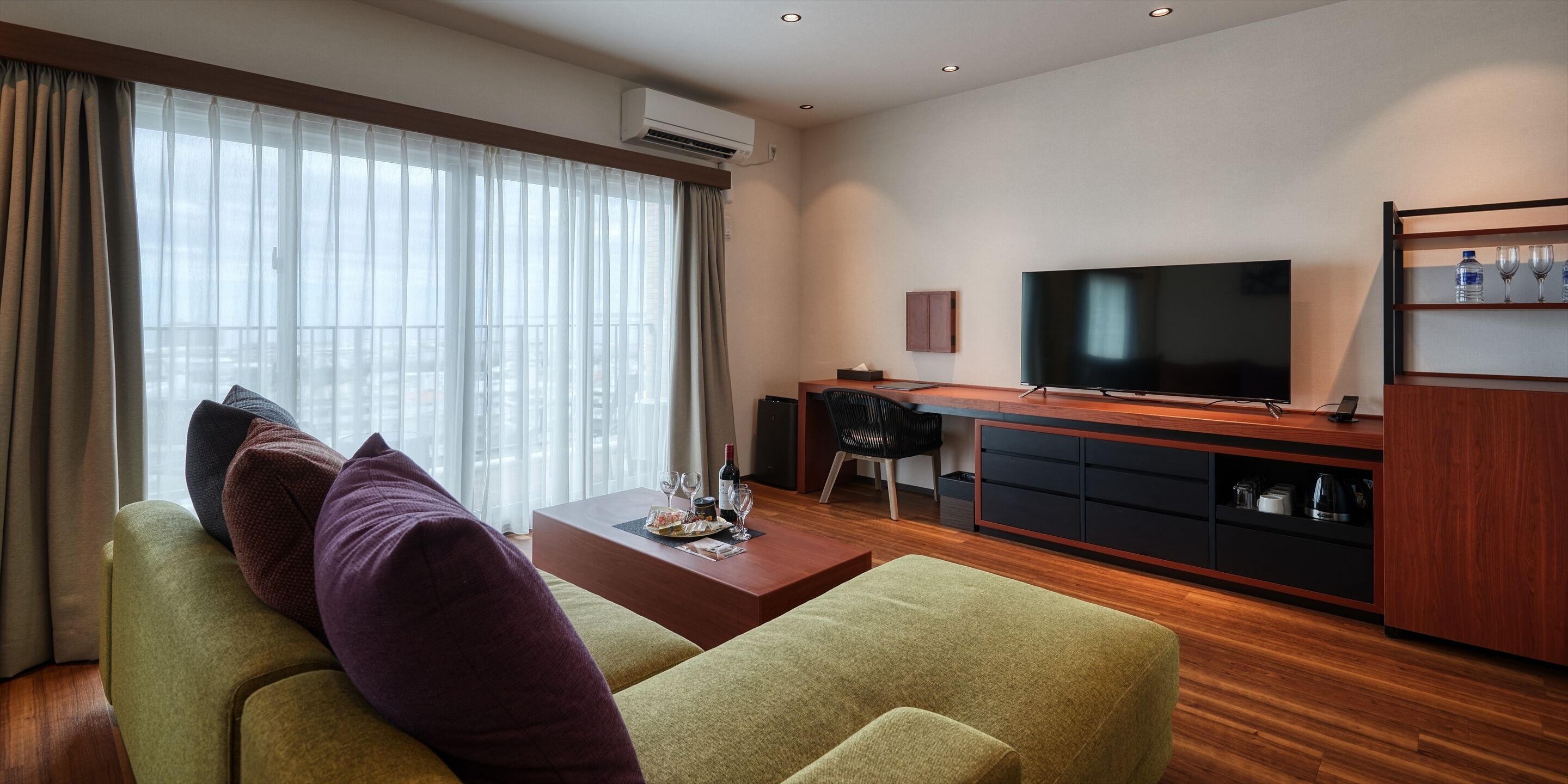 Una sala moderna con sofá, mesa de centro, televisor y una zona de cocina con televisor y estanterías.