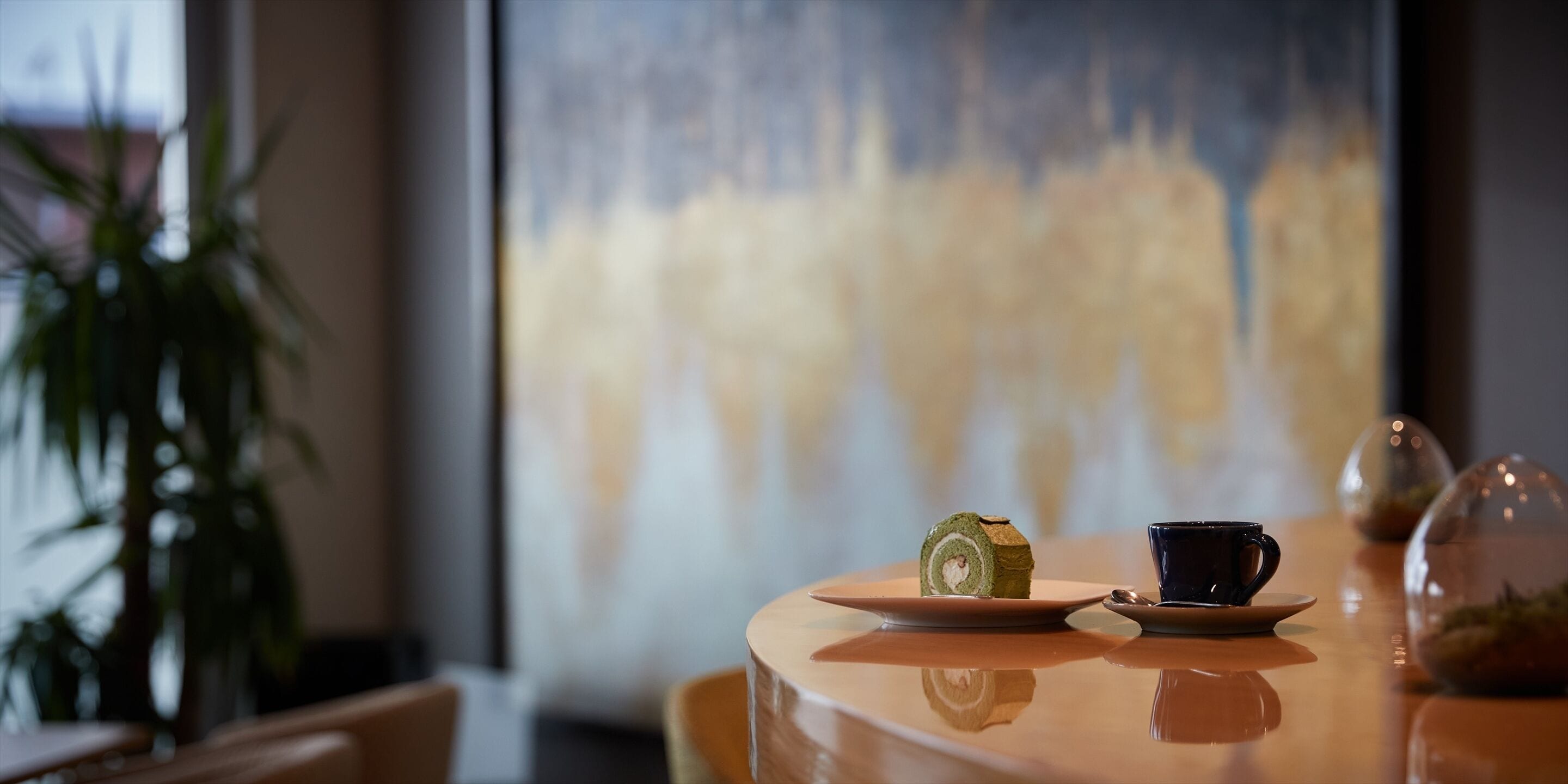 A table with a sushi roll, a black cup, and a glass dome containing a plant.