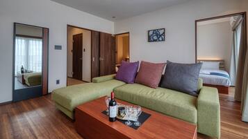 Een moderne hotelkamer met een groene bank, een houten bijzettafeltje met een fles en glazen, een bed met een blauw-witte dekbedovertrek en een grote spiegel.