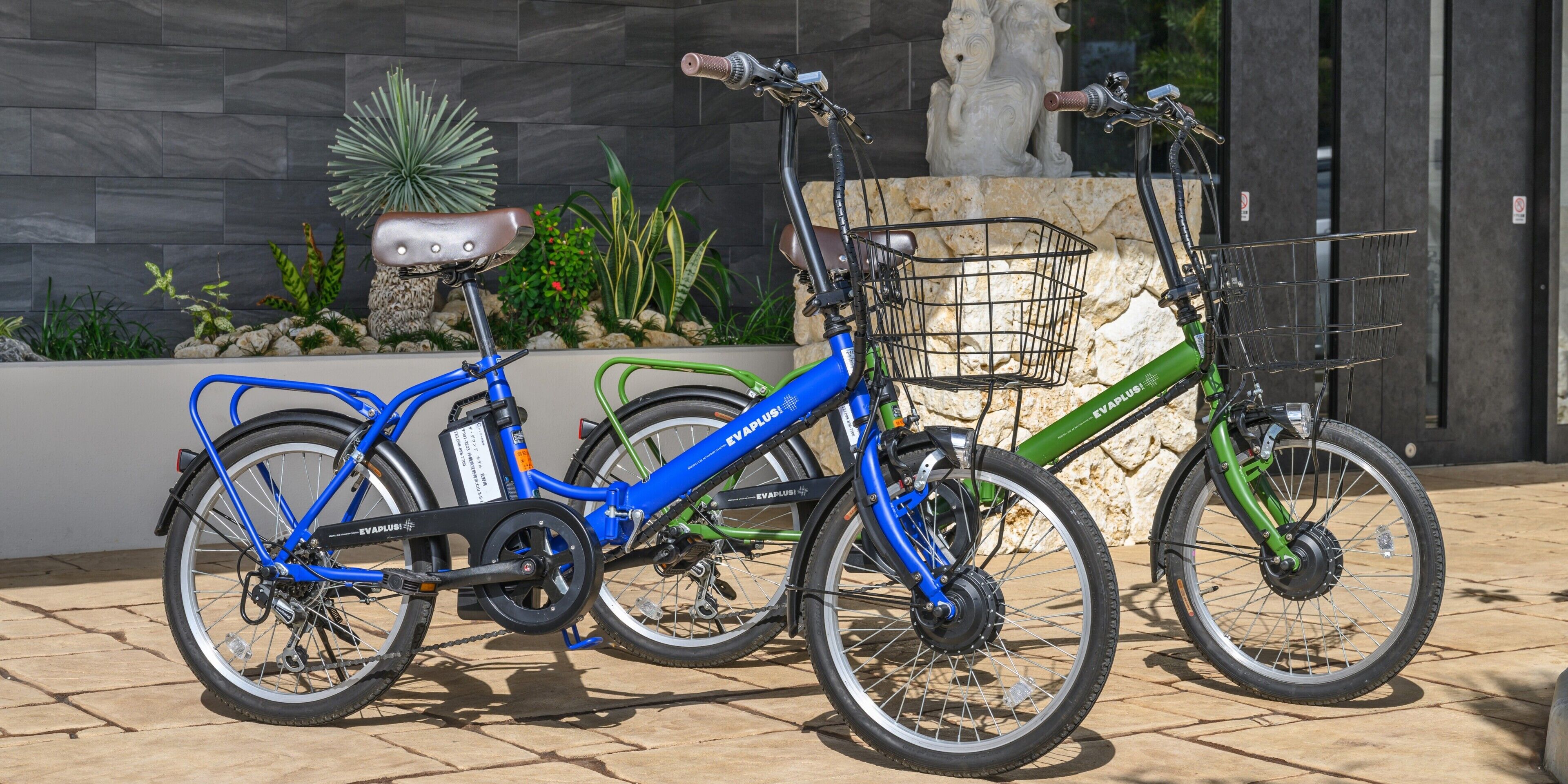 Dos bicicletas estacionadas frente a un edificio de fachada de piedra y un macetero con plantas.