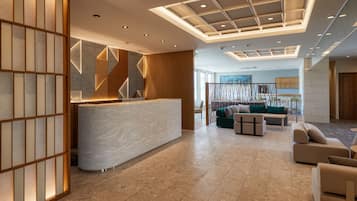 A modern reception area with a marble counter, geometric wall design, and a seating area with sofas and a coffee table.