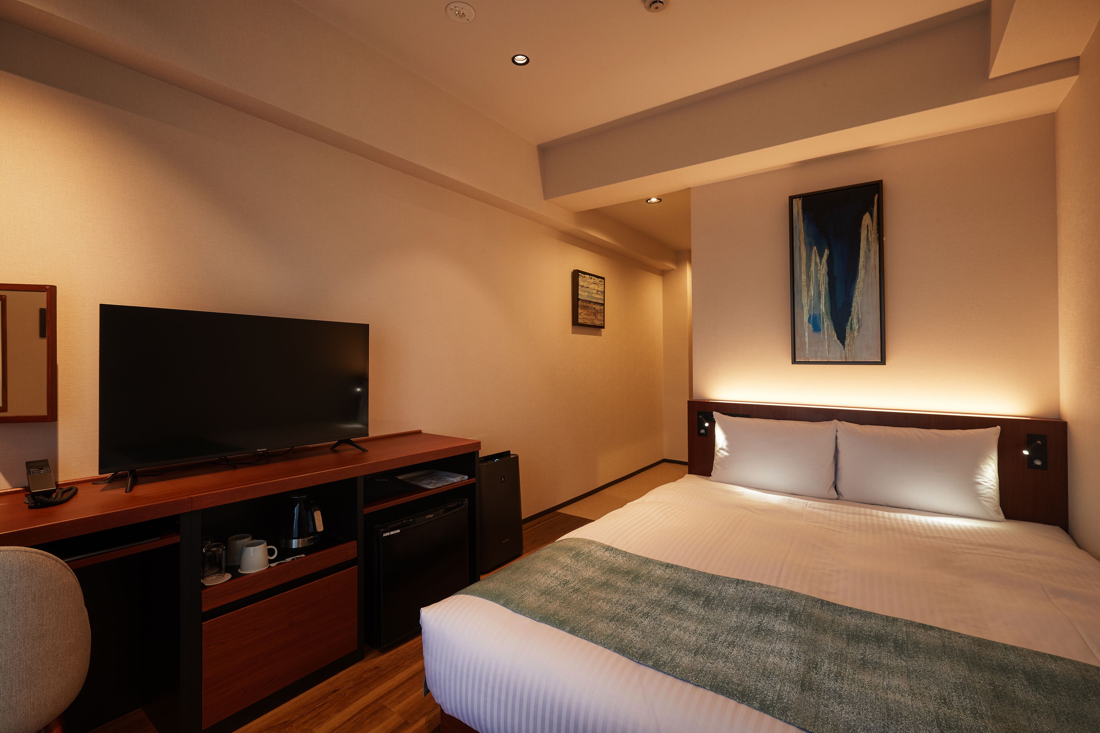 Quarto de hotel com uma cama grande, televisão de tela plana, escrivaninha com cafeteira e um quadro na parede.