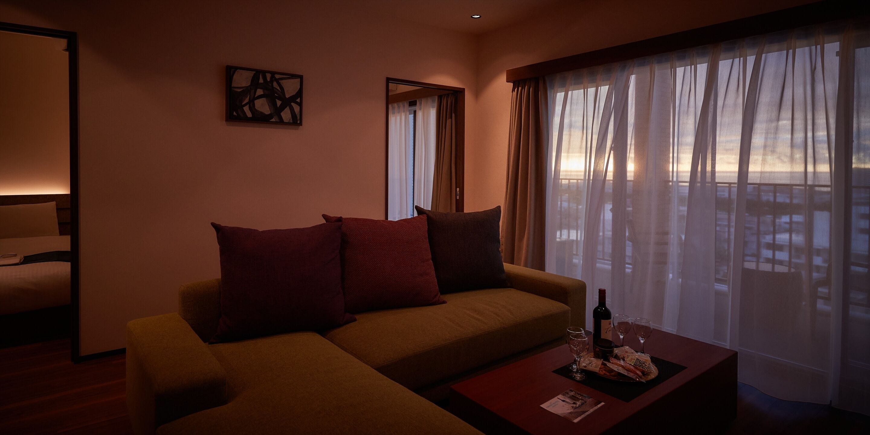 A modern living room with a sofa, a coffee table, and a view of the outdoors through sheer curtains.