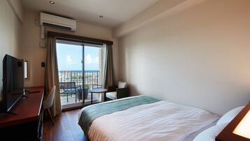 Habitación de hotel con cama, escritorio, silla, mesita pequeña y balcón con vistas.