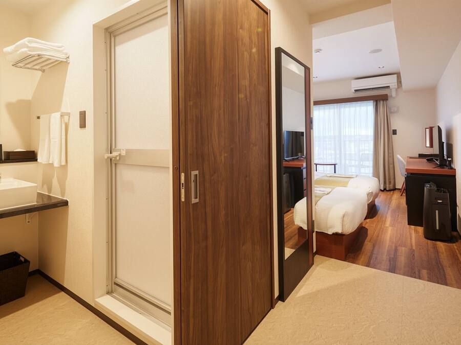 A hotel room with a bathroom, a bed, a desk, and a TV.