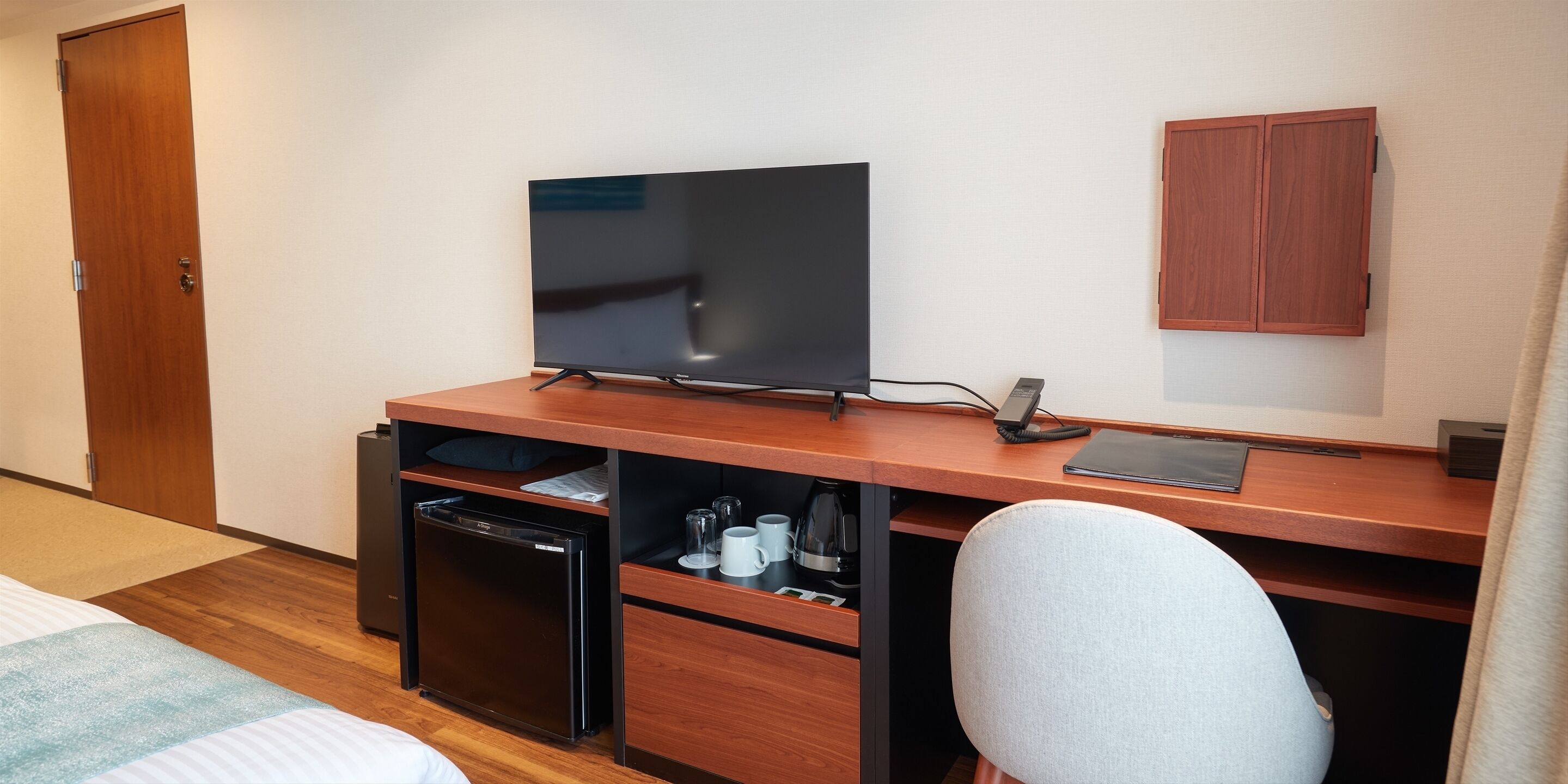A hotel room with a wooden desk, a television, a mini-fridge, a coffee maker, and a cabinet.