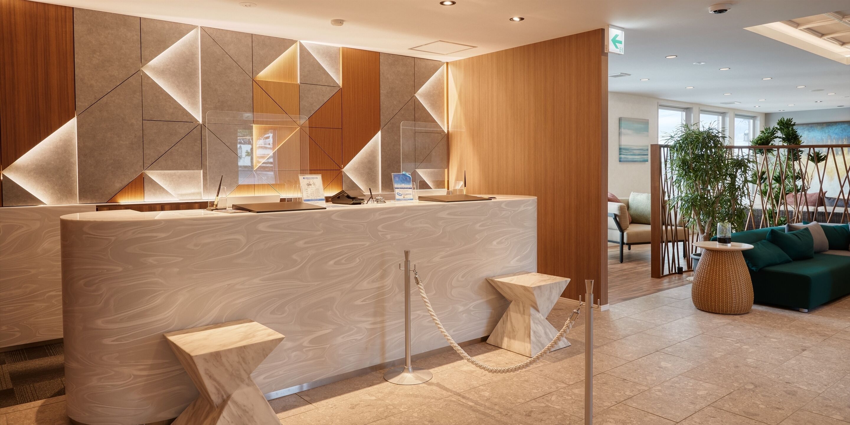 A modern reception area with a geometric wall design, a reception desk, and a seating area with a green sofa and a plant.